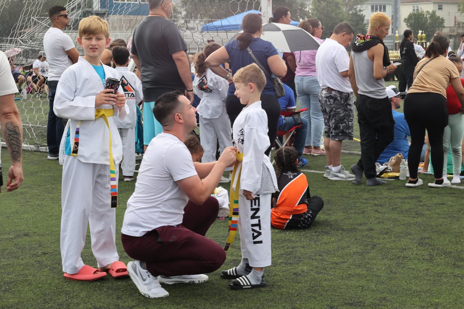 Dad kneeling to fix his child's belt at a ZENTAI Martial Arts belt promotion in New Jersey