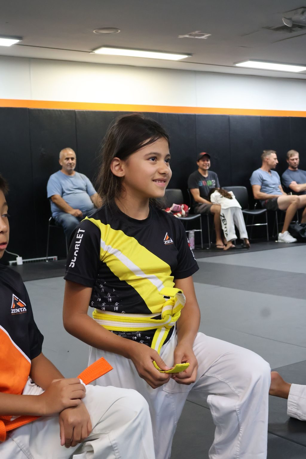 Smiling girl in uniform sitting on the mat at ZENTAI Martial Arts in North Arlington, NJ
