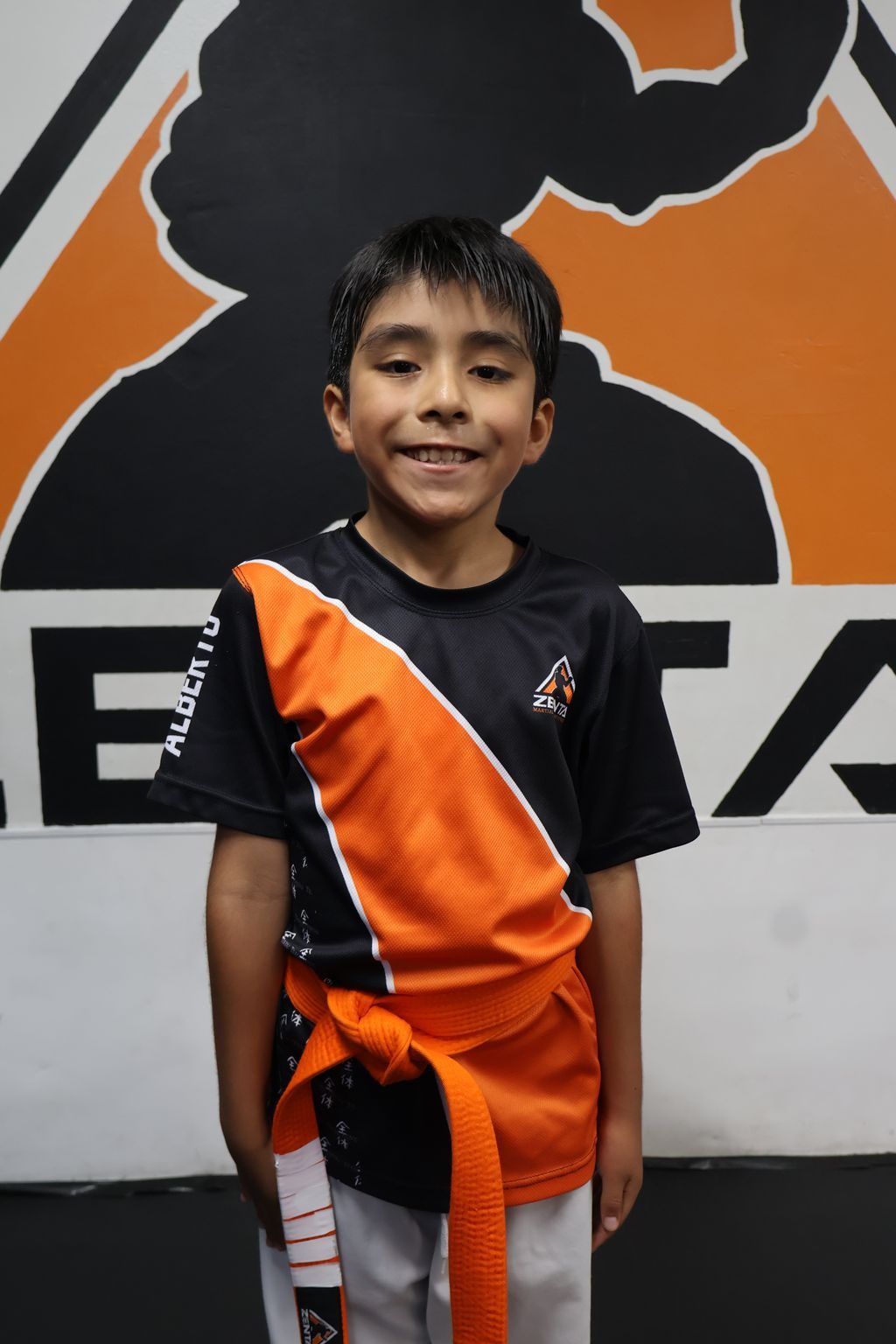 Boy smiling in front of the ZENTAI logo at ZENTAI Martial Arts in North Arlington, NJ
