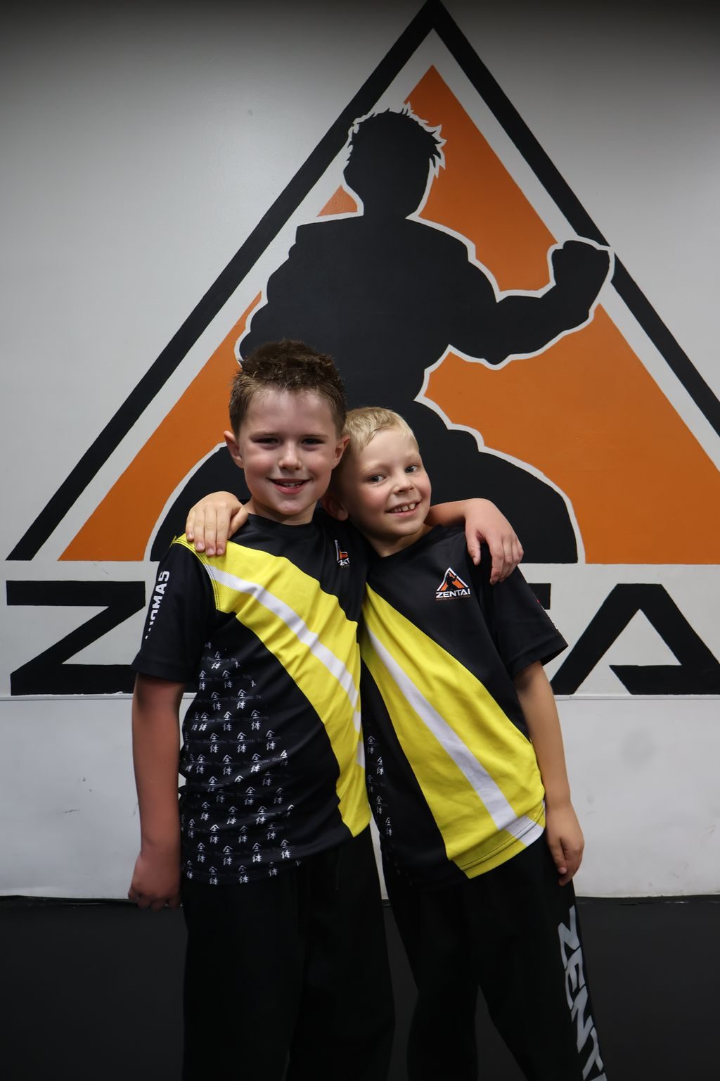 Two kids hugging in front of the ZENTAI logo at ZENTAI Martial Arts in North Arlington, NJ