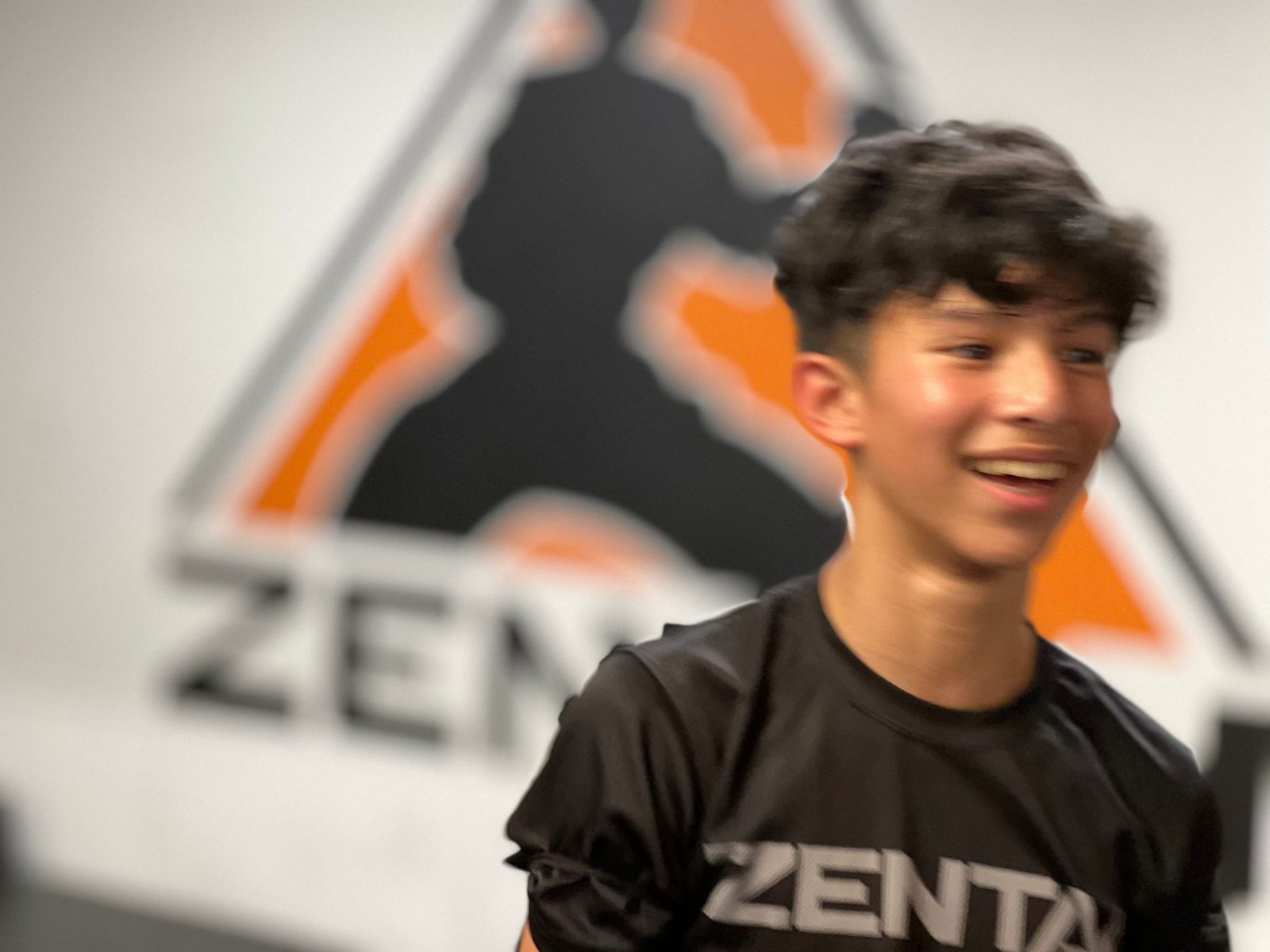 Teen smiling in front of the ZENTAI logo at ZENTAI Martial Arts in New Jersey